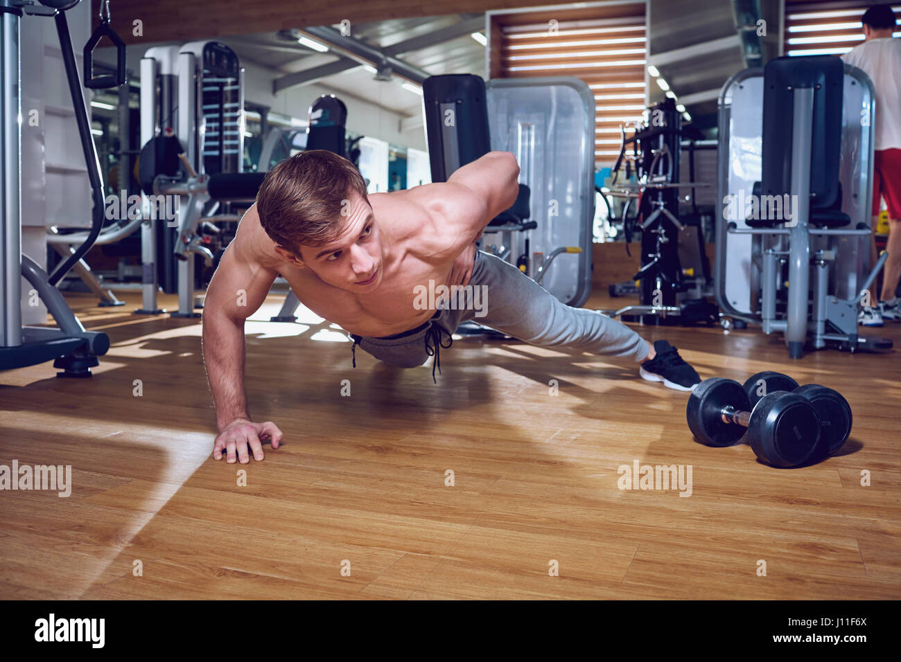 Sport-Typ macht Liegestütze aus dem Boden auf der einen Seite im Fitness-Studio Stockfoto