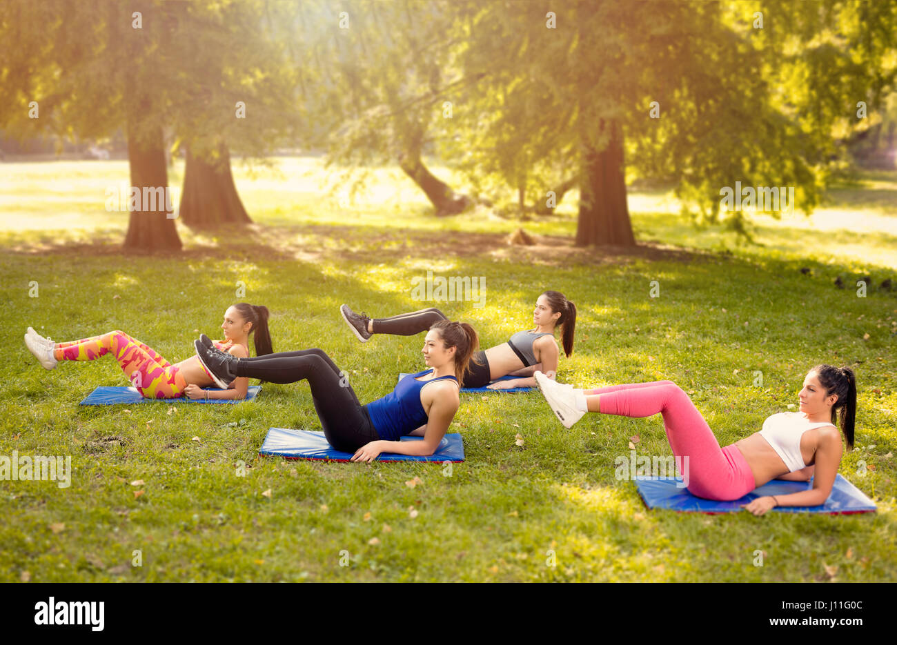 Vier schöne Freundinnen tun tut Sit-up im Park. Stockfoto