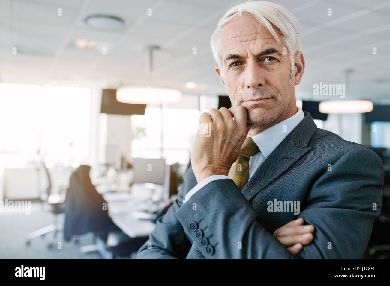 Porträt von reifer Geschäftsmann im Büro stehen und starrte in die Kamera. Nachdenklich senior Professional mit Hand am Kinn. Stockfoto