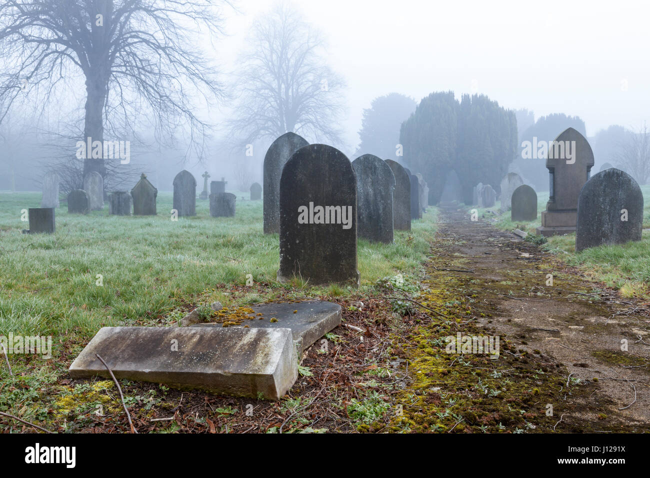 Gefallenen Grabstein und andere Grabsteine auf einem nebligen Tag auf einem Friedhof, England, Großbritannien Stockfoto