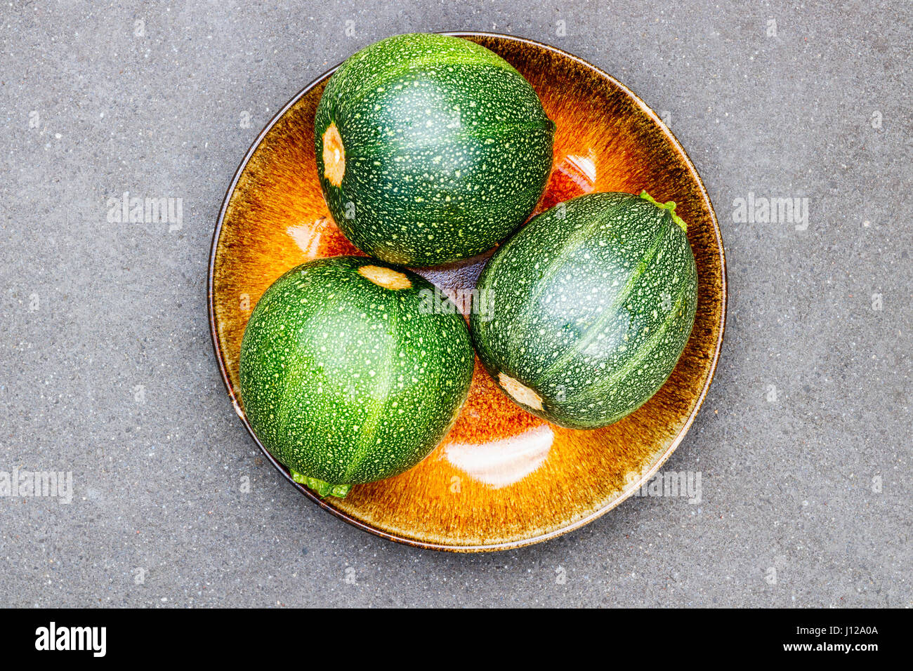 Drei runde Zucchini auf ein gelbes Schild mit grauem Hintergrund Stockfoto