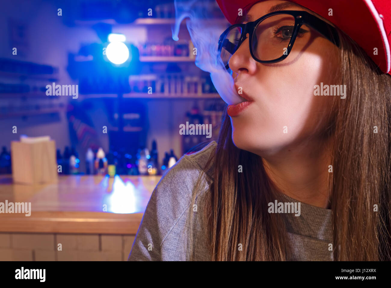 Junge hübsche Frau im roten Mütze Rauch eine elektronische Zigarette im Vaporizer Shop. Closeup. Stockfoto