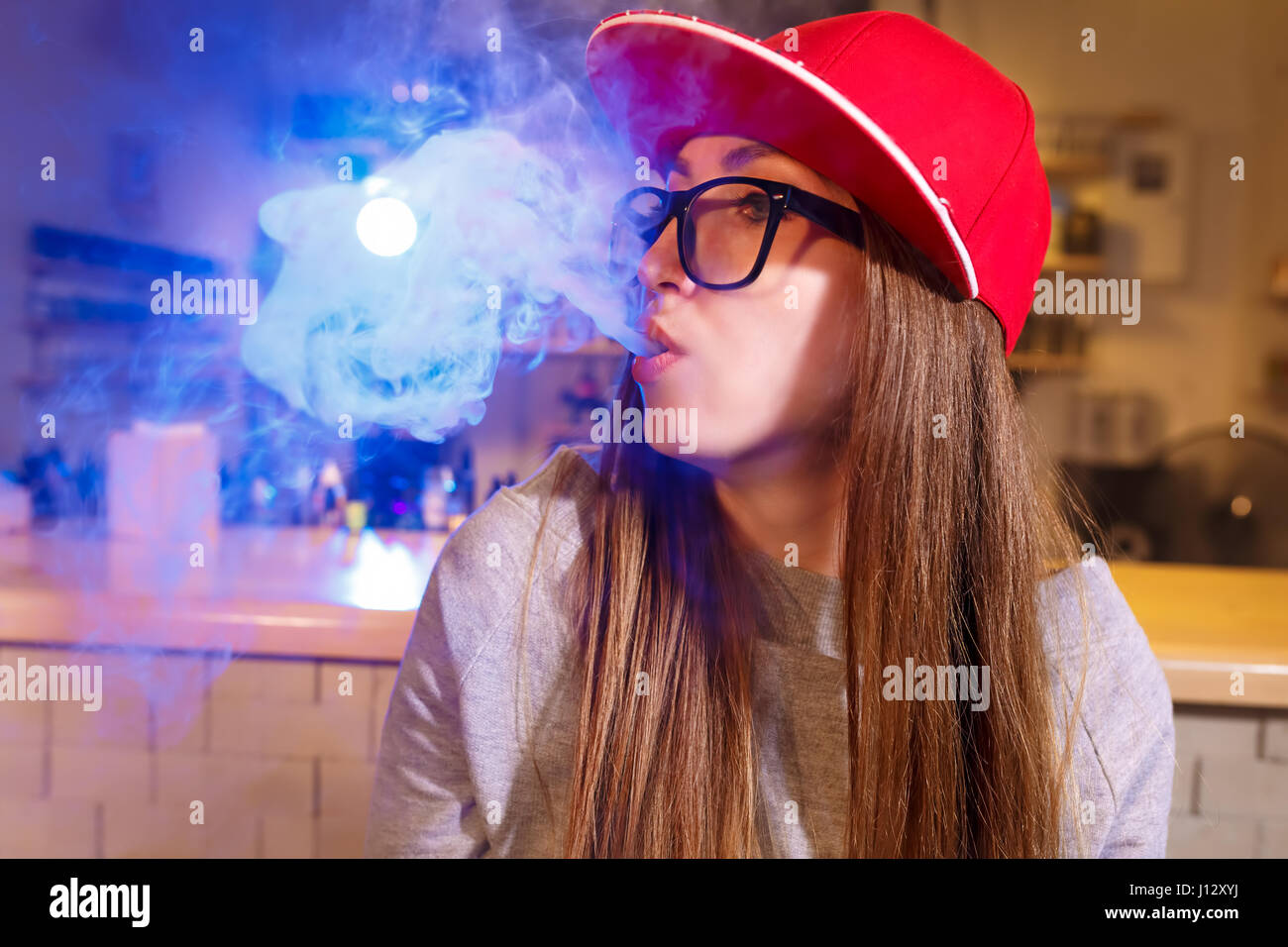 Junge hübsche Frau im roten Mütze Rauch eine elektronische Zigarette im Vaporizer shop Stockfoto