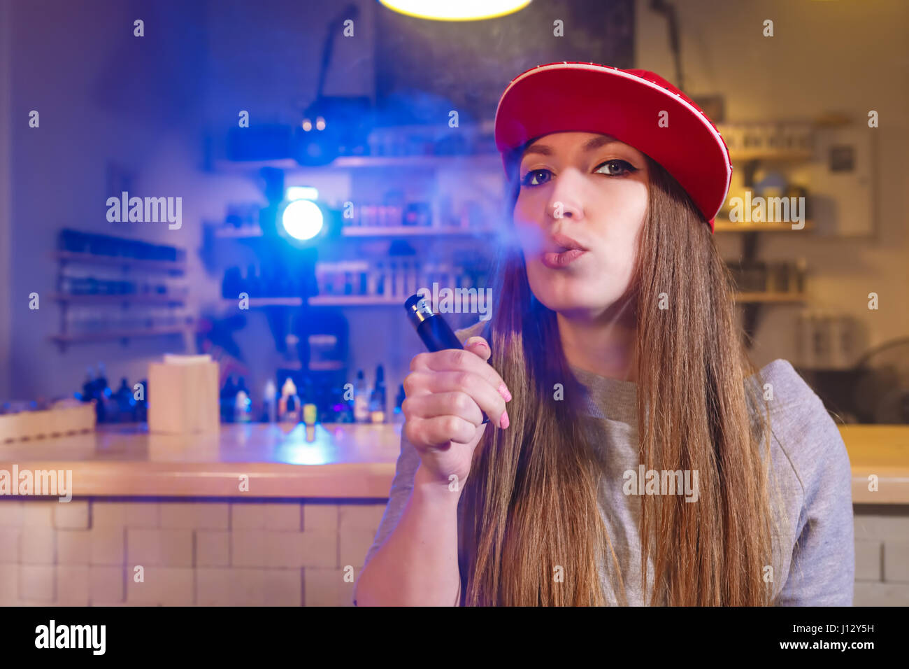 Junge hübsche Frau im roten Mütze Rauch eine elektronische Zigarette im Vaporizer shop Stockfoto