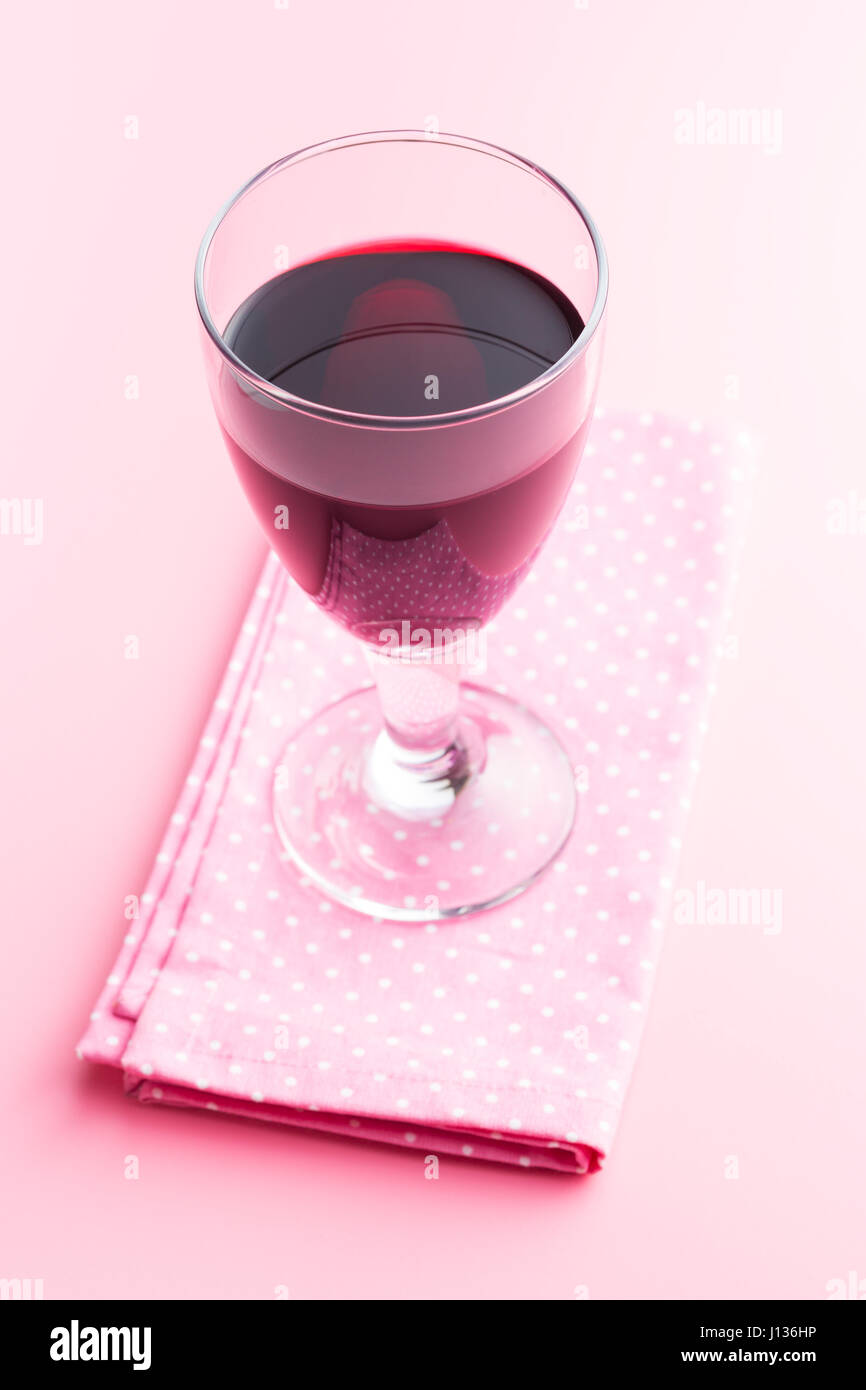 Glas Rotwein auf rosa Hintergrund mit Serviette. Stockfoto