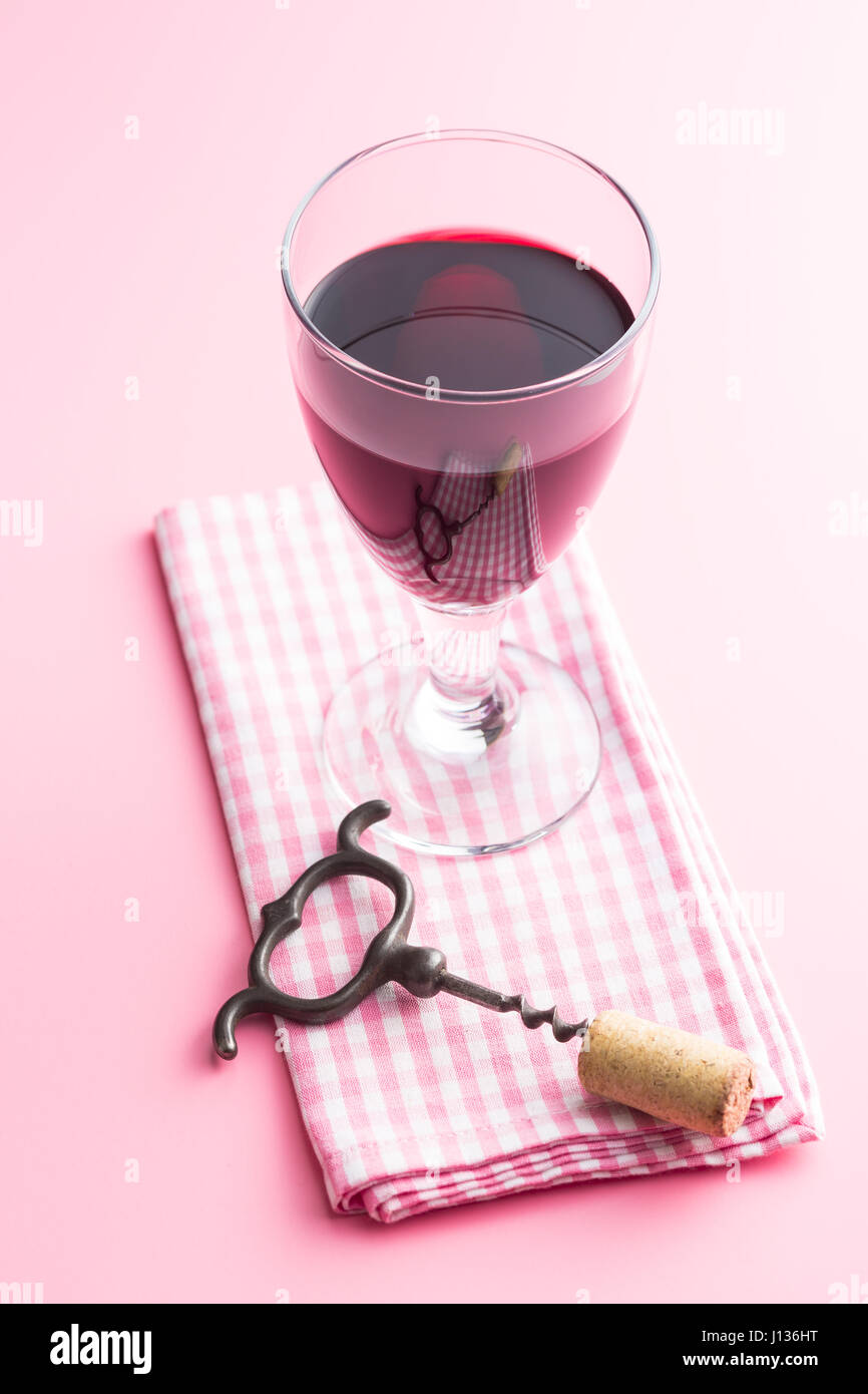 Glas Rotwein auf rosa Hintergrund mit Serviette, Korkenzieher und Kork. Stockfoto