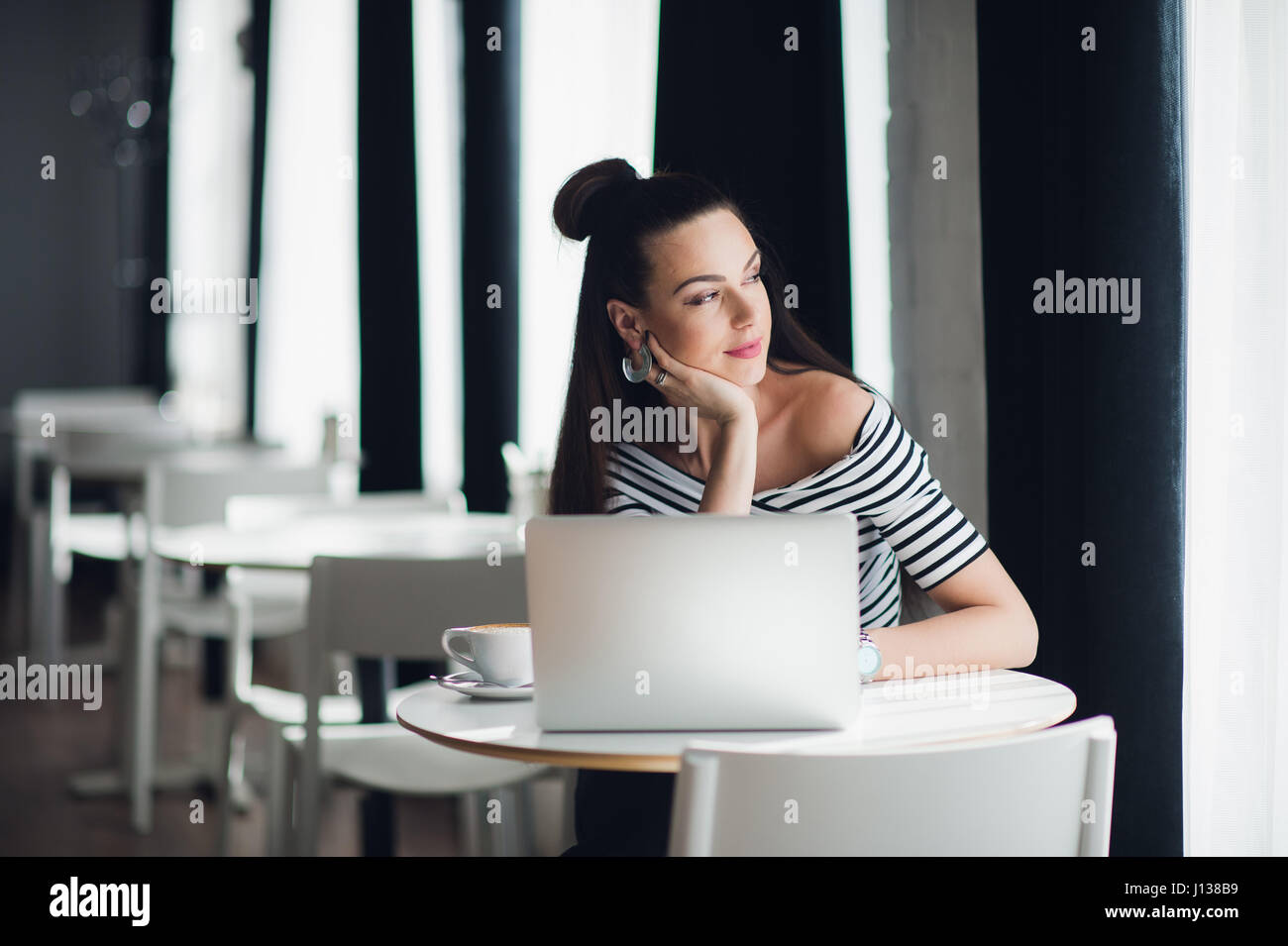 Porträt von einer attraktiven Frau in einigen Coffee-Shop mit ihrem Laptop sitzen und denken über ein Thema beim Blick durch das Fenster. Stockfoto