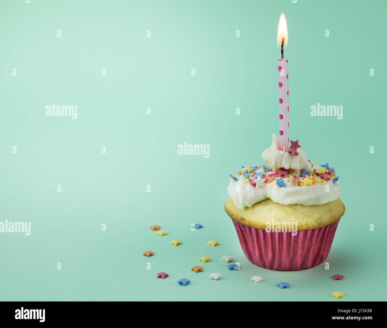 Ein Cupcake mit brennenden Kerze und Sterne Streusel auf grünem Hintergrund isoliert Stockfoto