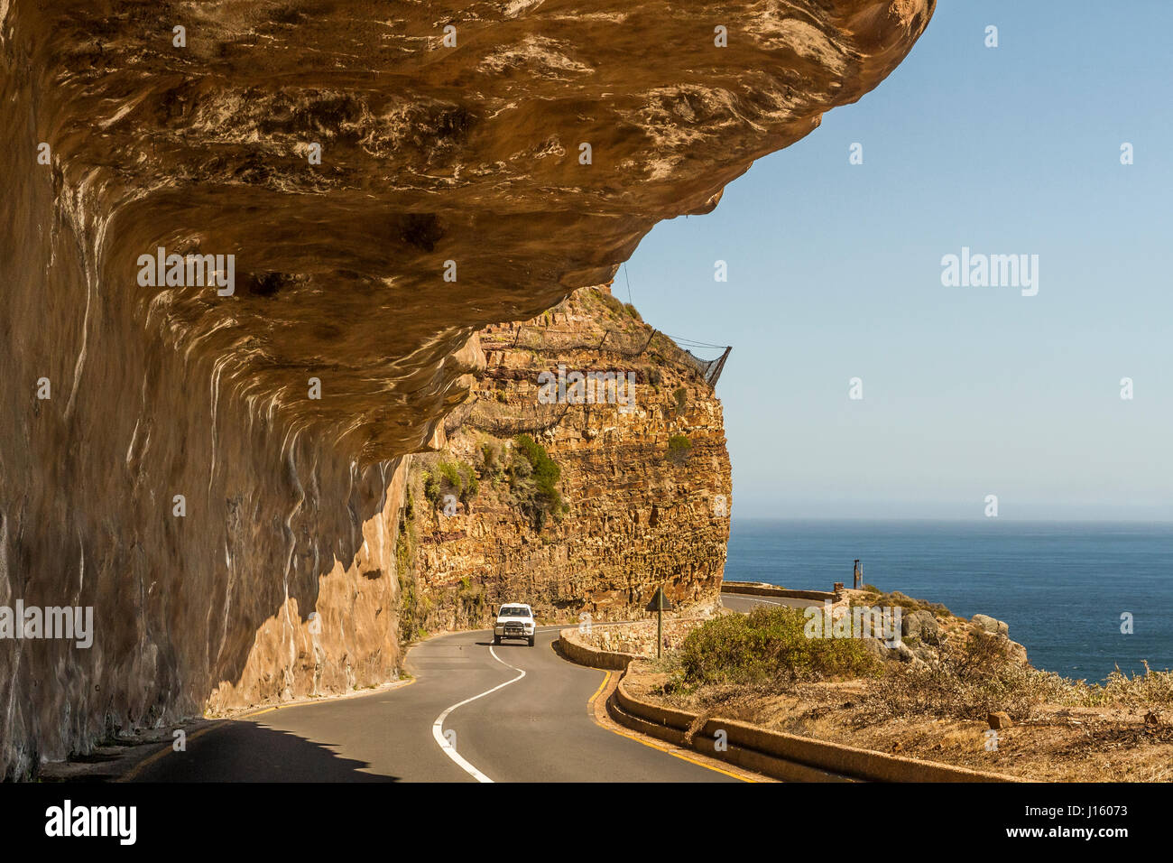 Ein Auto fährt unter der überhängenden Klippen des Chapman's Peak Drive, eine spektakuläre landschaftliche Oceanside Drive in der Nähe von Kapstadt Südafrika Stockfoto