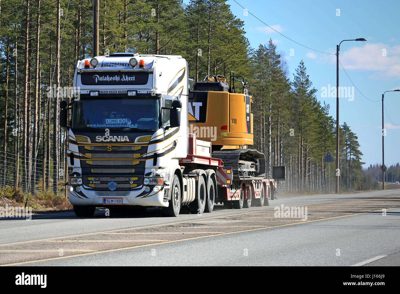 LOUKKU, Finnland - 2. April 2016: Scania R560 V8 Lkw schleppt CAT 325F L Medium Hydraulikbagger Highway entlang. Stockfoto