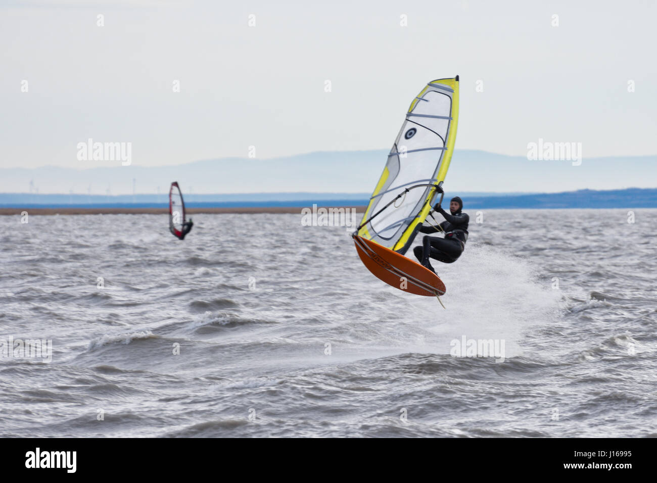 Windsurfer auf dem Neusiedlersee (Neusiedler See) einen Sprung bei starkem Wind und Wellen. Kaltes Wetter, bewölkter Himmel Stockfoto