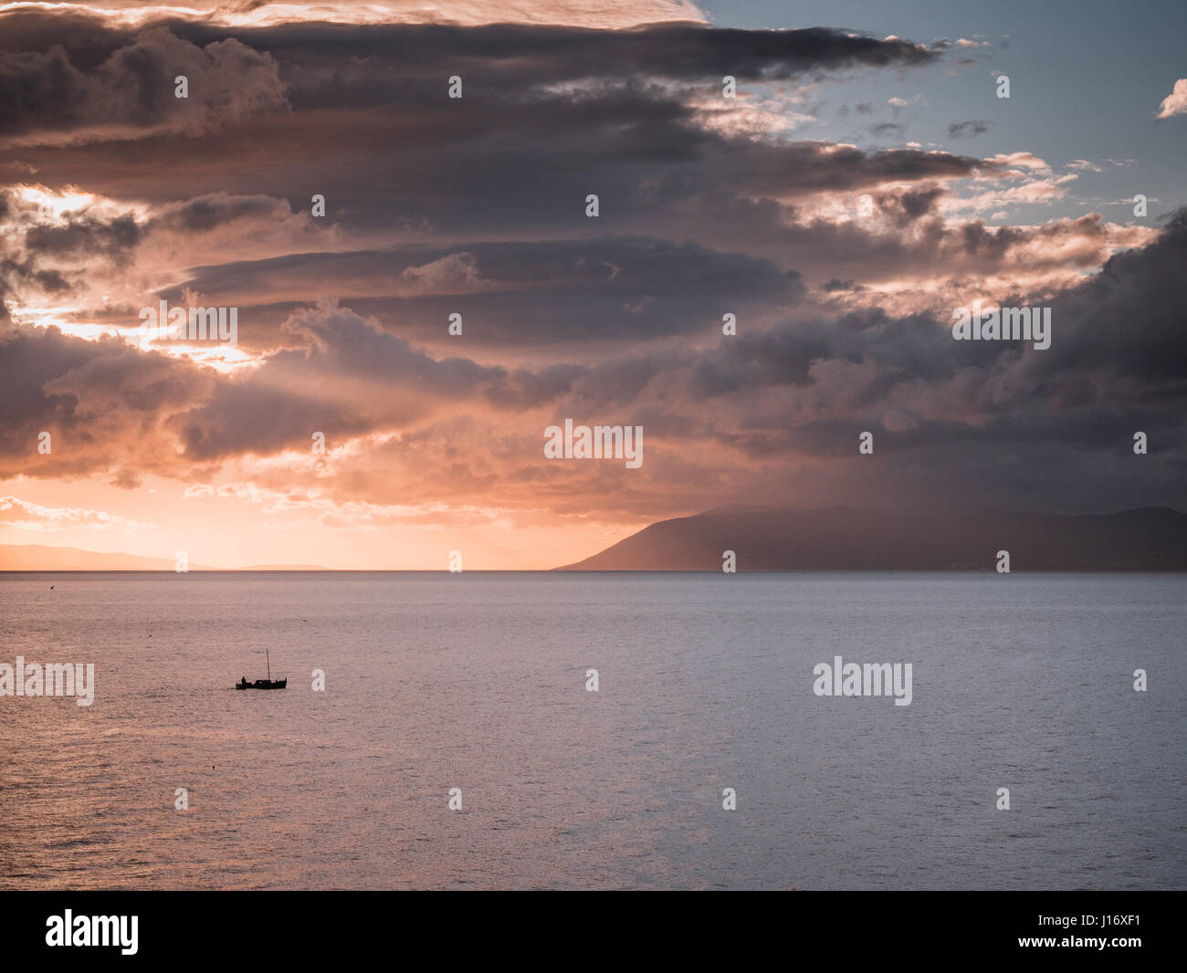 Kleines Boot Segeln auf dem Meer bei Sonnenuntergang mit großen Wolken Stockfoto