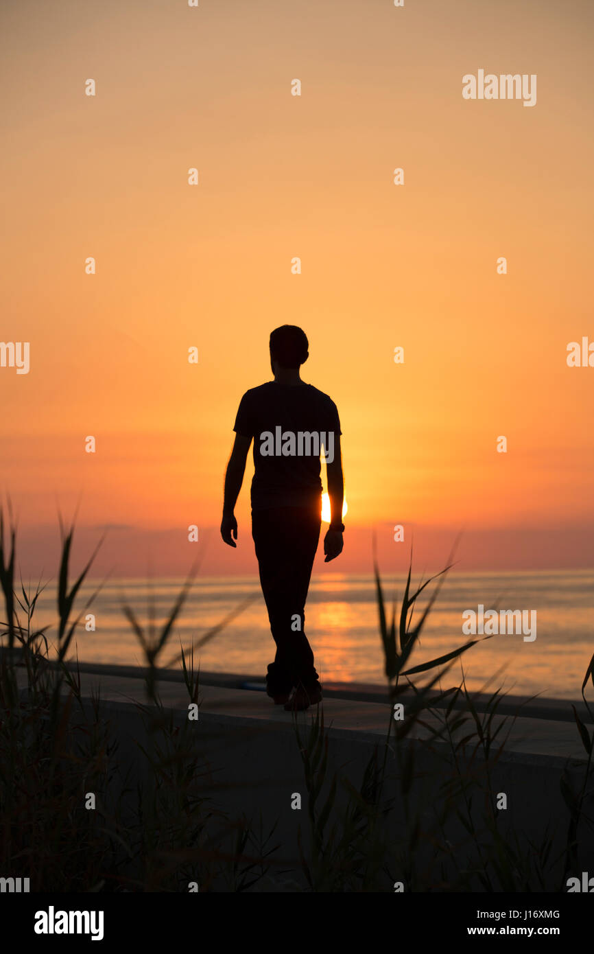 Voller Länge Silhouette einer männlichen Figur, die zu Fuß am Strand bei Sonnenuntergang Stockfoto