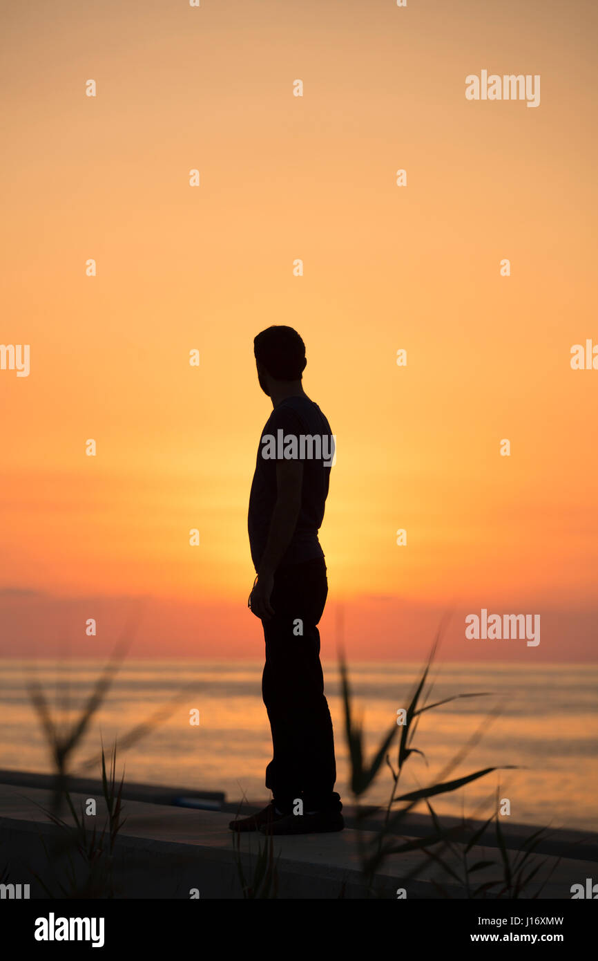 Silhouette einer männlichen Figur stehen am Strand bei Sonnenuntergang Stockfoto