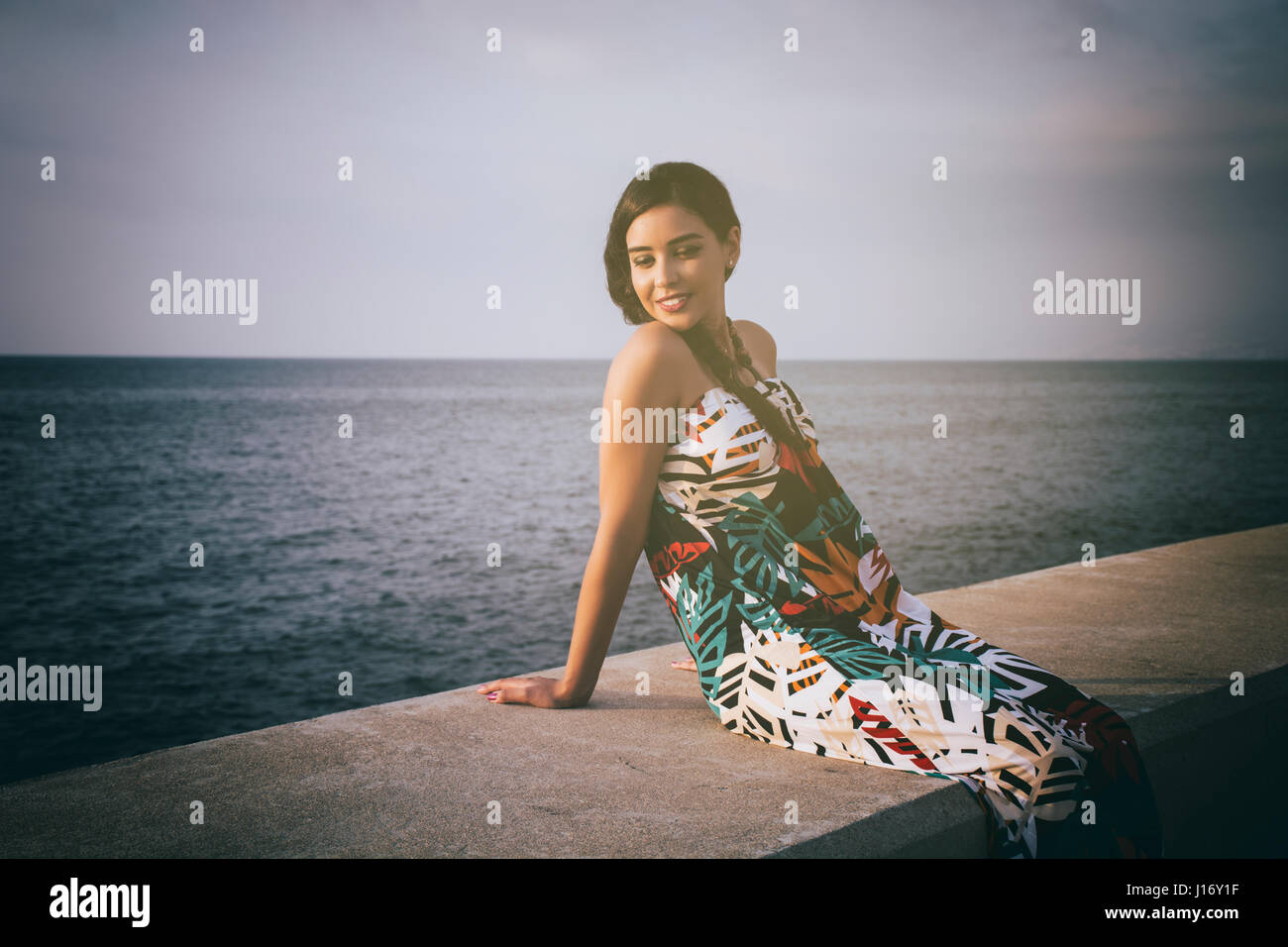Glückliche junge Frau setzte sich an das Meer Lächeln auf den Lippen Stockfoto