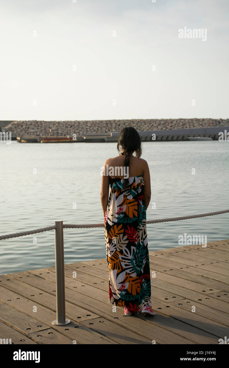 Rückansicht einer Frau trägt ein Sommerkleid, stehend auf dem Kai am Meer Stockfoto