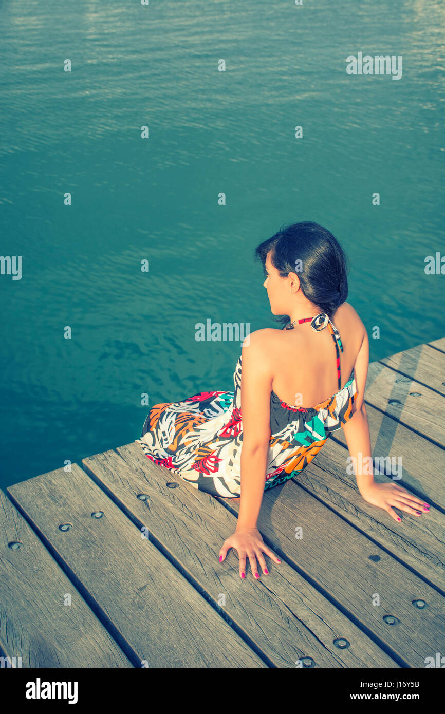 Rückansicht einer jungen Frau saß auf dem Kai am Meer Stockfoto