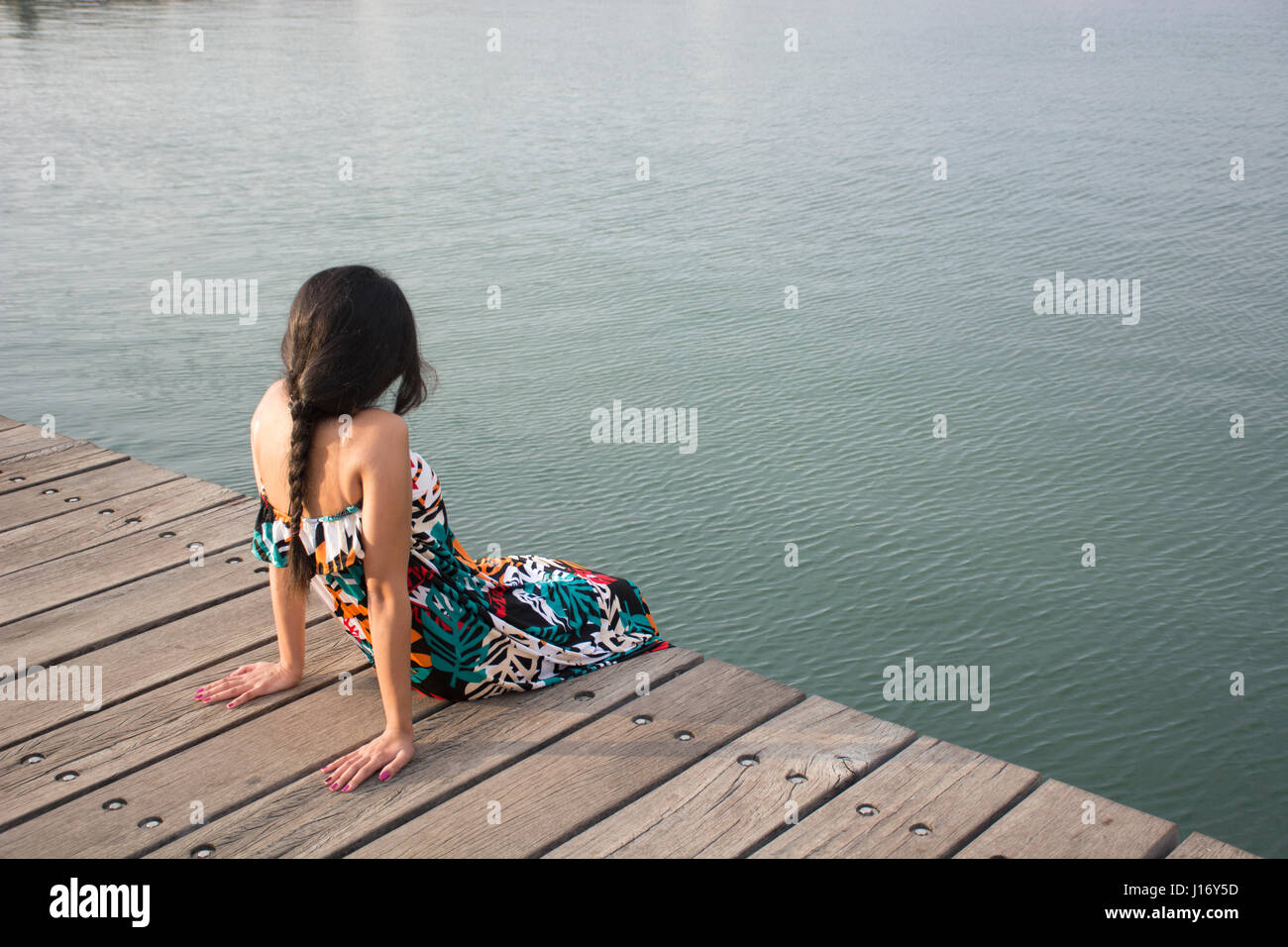 Rückansicht einer jungen Frau saß auf dem Kai am Meer Stockfoto