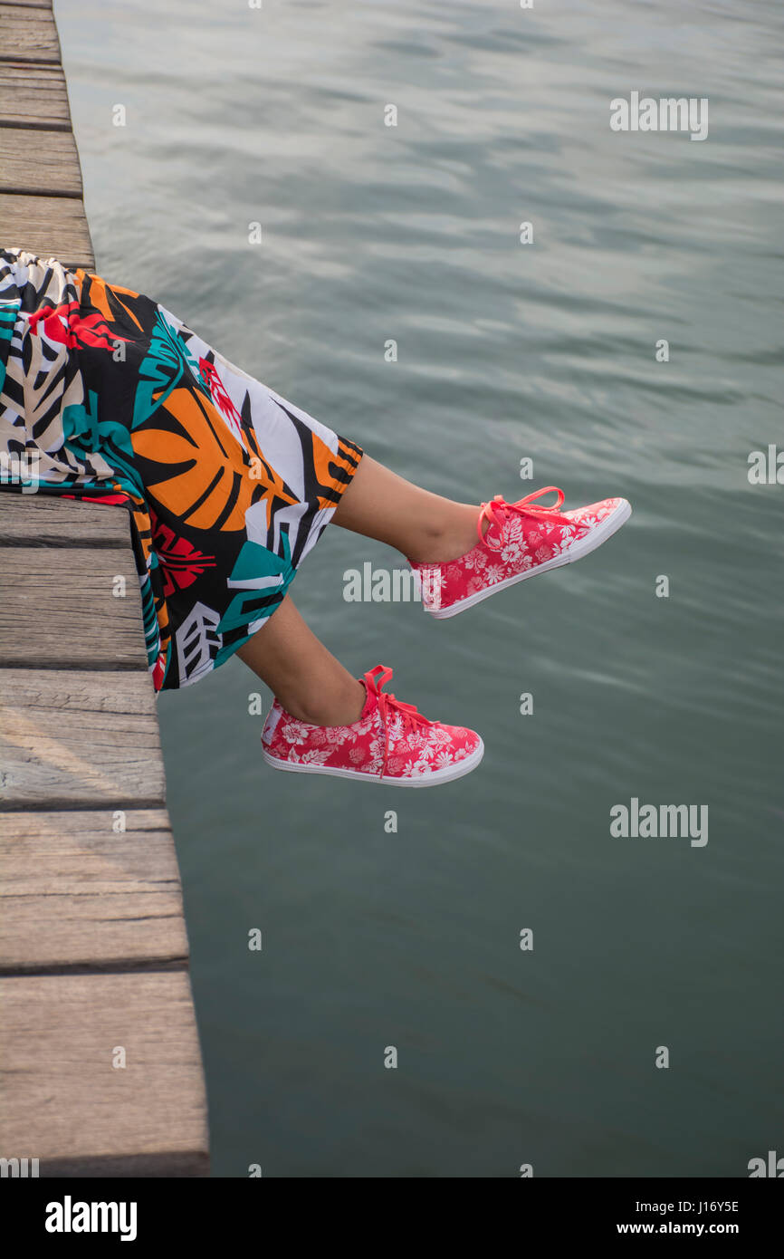 Nahaufnahme von einer jungen Frau Füße sitzen auf dem Kai am Meer Stockfoto