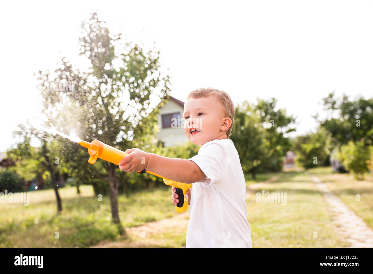 Kleiner Junge mit Wasserpistole spritzt jemand, sonnigen Sommer garde Stockfoto