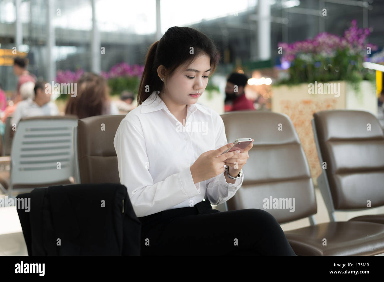 Junge asiatische Geschäftsfrau mit Smartphone beim Sitzen im Flughafen-Terminal für das Boarding warten. Stockfoto
