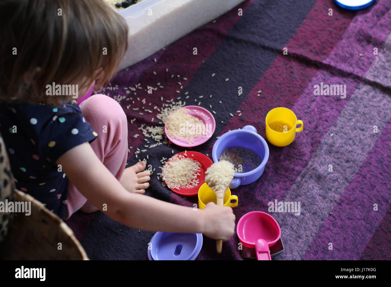 von kleinen Mädchen spielen mit Reis und Spielzeug Teller, Tassen und Löffel, sensorische spielen hautnah Stockfoto