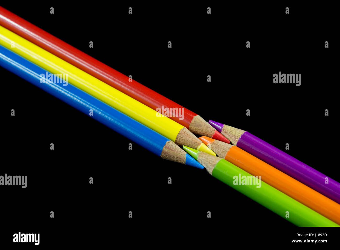 Drei primäre Buntstifte mit Blick auf drei sekundären Buntstifte mit einem dunklen schwarzen Hintergrund. Stockfoto