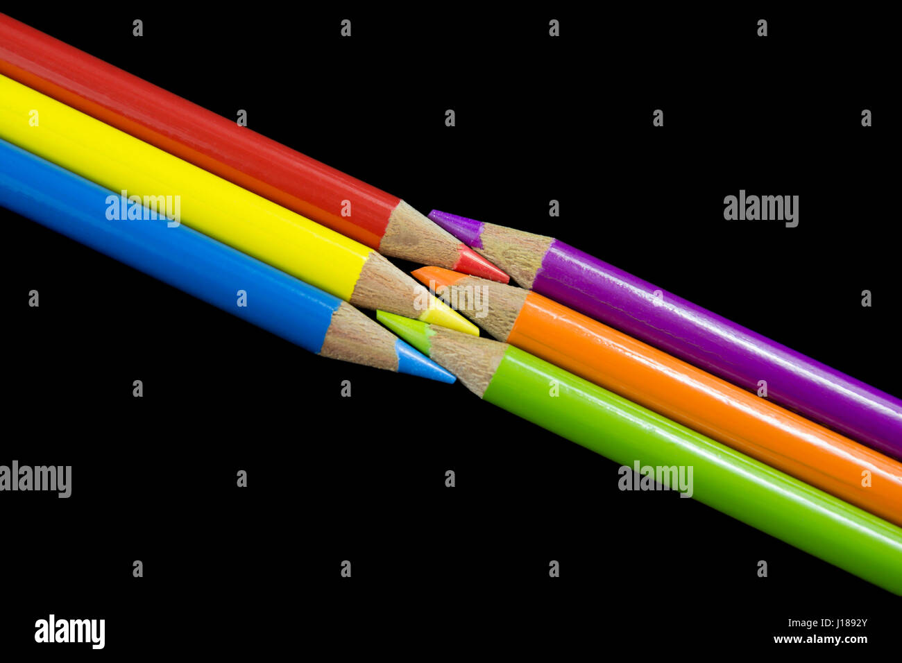 Drei primäre Buntstifte mit Blick auf drei sekundären Buntstifte mit einem dunklen schwarzen Hintergrund. Stockfoto