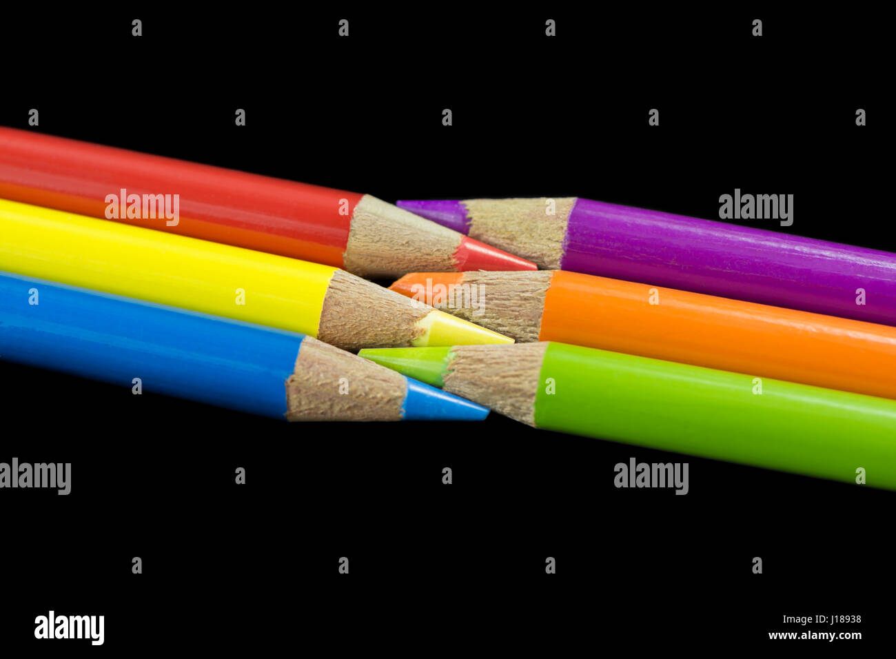 Drei primäre Buntstifte mit Blick auf drei sekundären Buntstifte mit einem dunklen schwarzen Hintergrund. Stockfoto