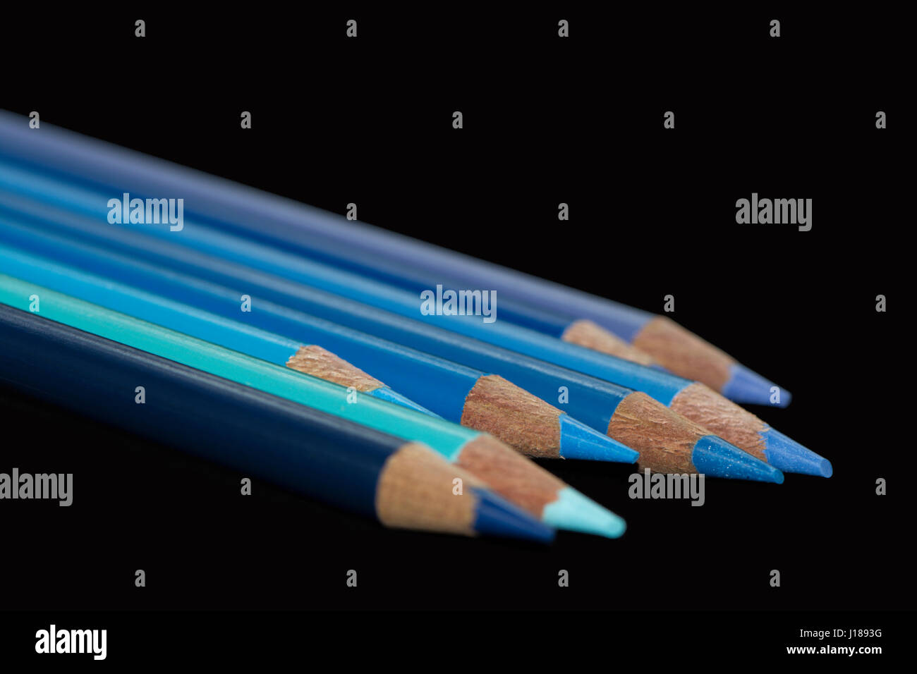 Acht blauen Farbstifte verschiedener Farbtöne und Schattierungen aufgereiht mit gestaffelten Längen mit einem dunklen schwarzen Hintergrund. Stockfoto