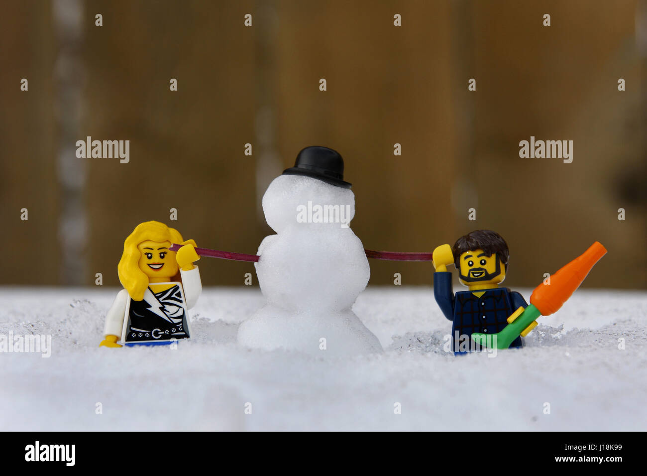 Männliche und weibliche Lego-Figuren, die im Winter einen Schneemann bauen Stockfoto