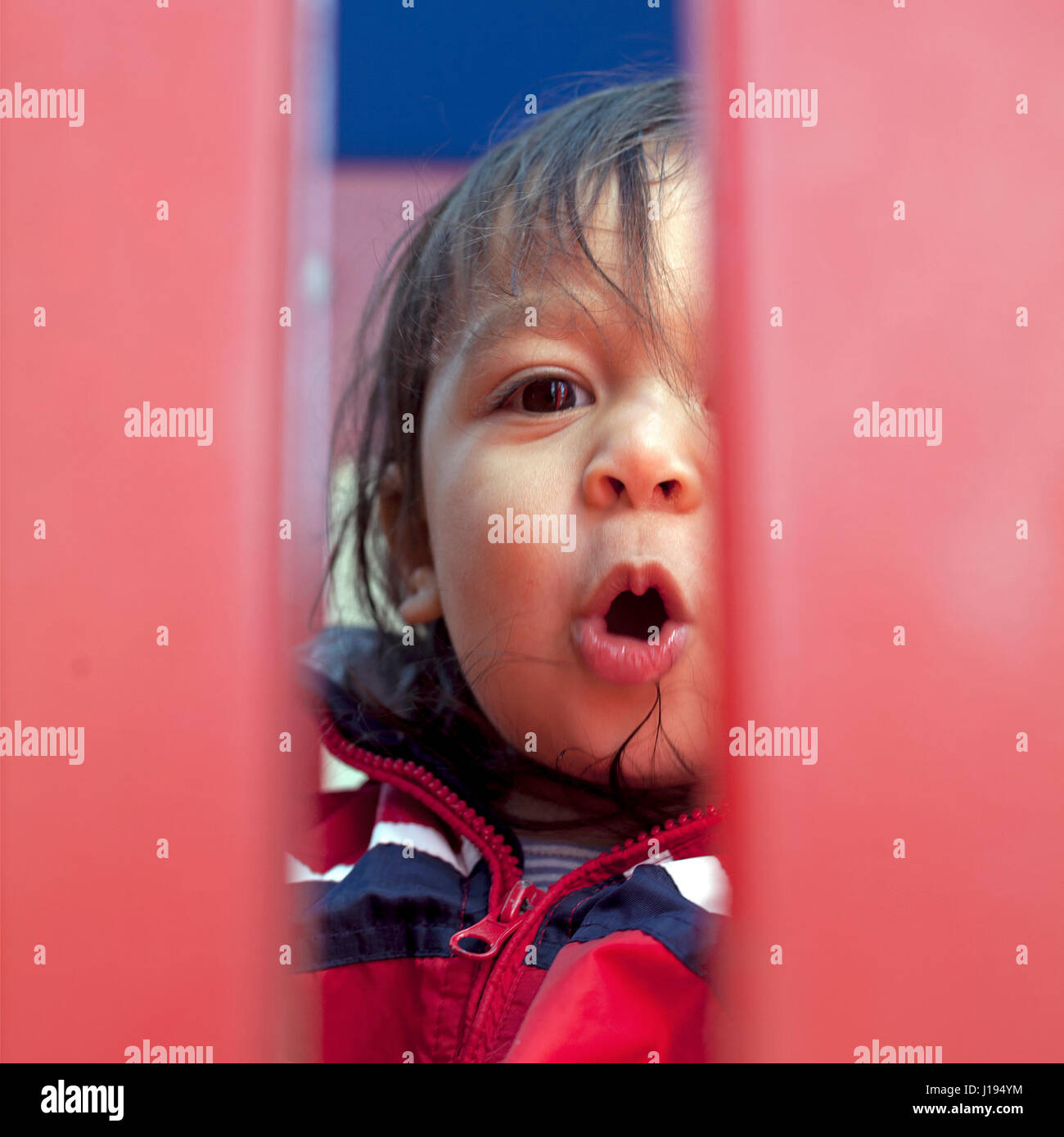 Ein junges Mädchen schaut durch eine Öffnung auf einem Spielplatz. Stockfoto