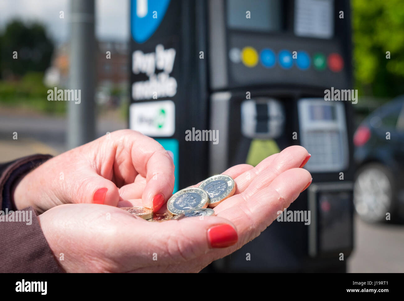 Eine Frau hält neue ein Pfund-Münzen an einem Parkplatz Zahlung Automaten Stockfoto