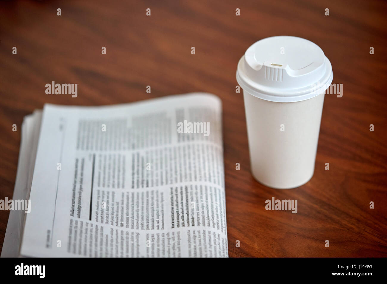 Kaffee trinken in Pappbecher und Zeitung auf Tisch Stockfoto