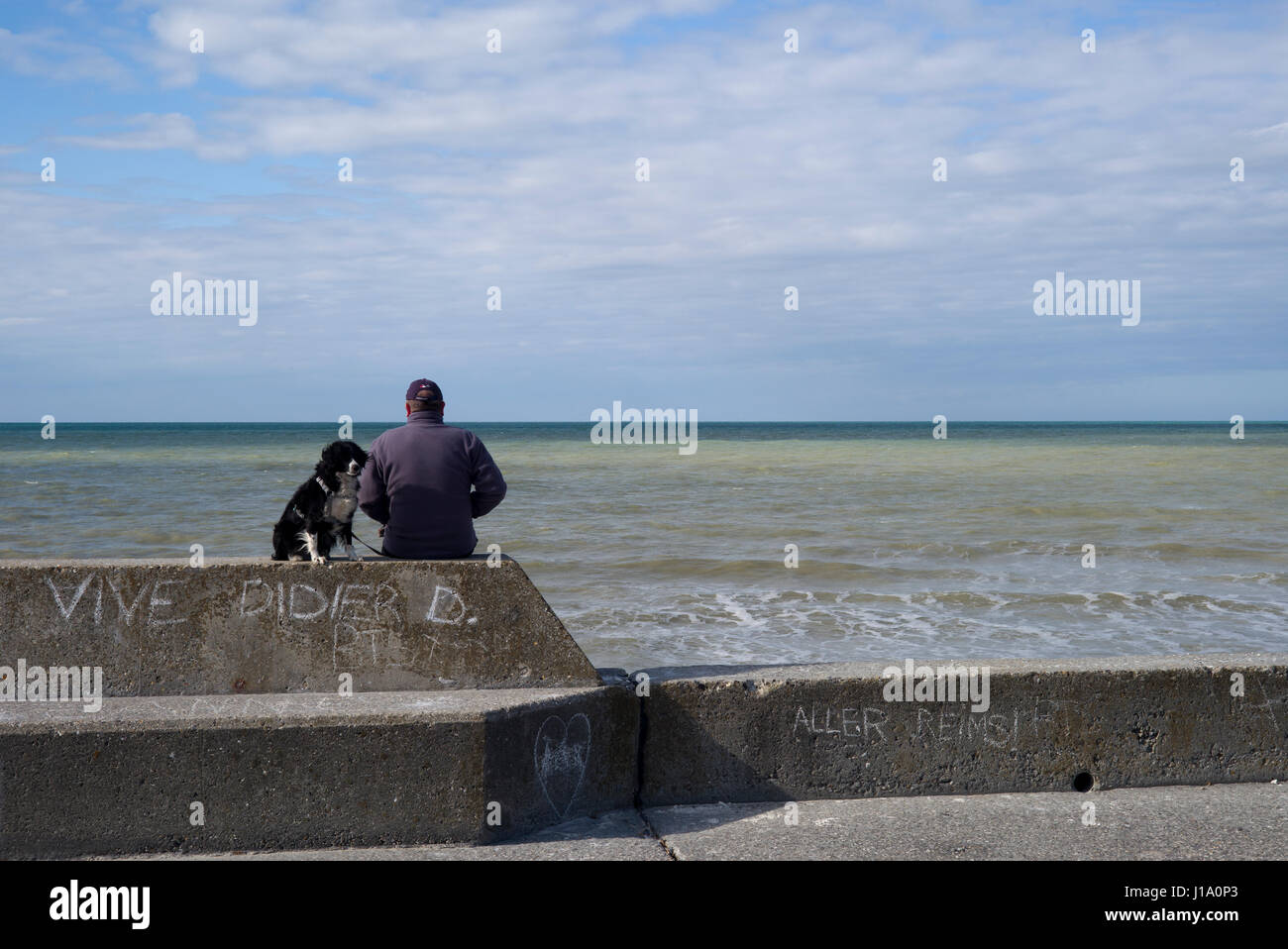Mann mit Hund sitzt am Deich mit Blick auf das Meer, Normandie, Frankreich Stockfoto