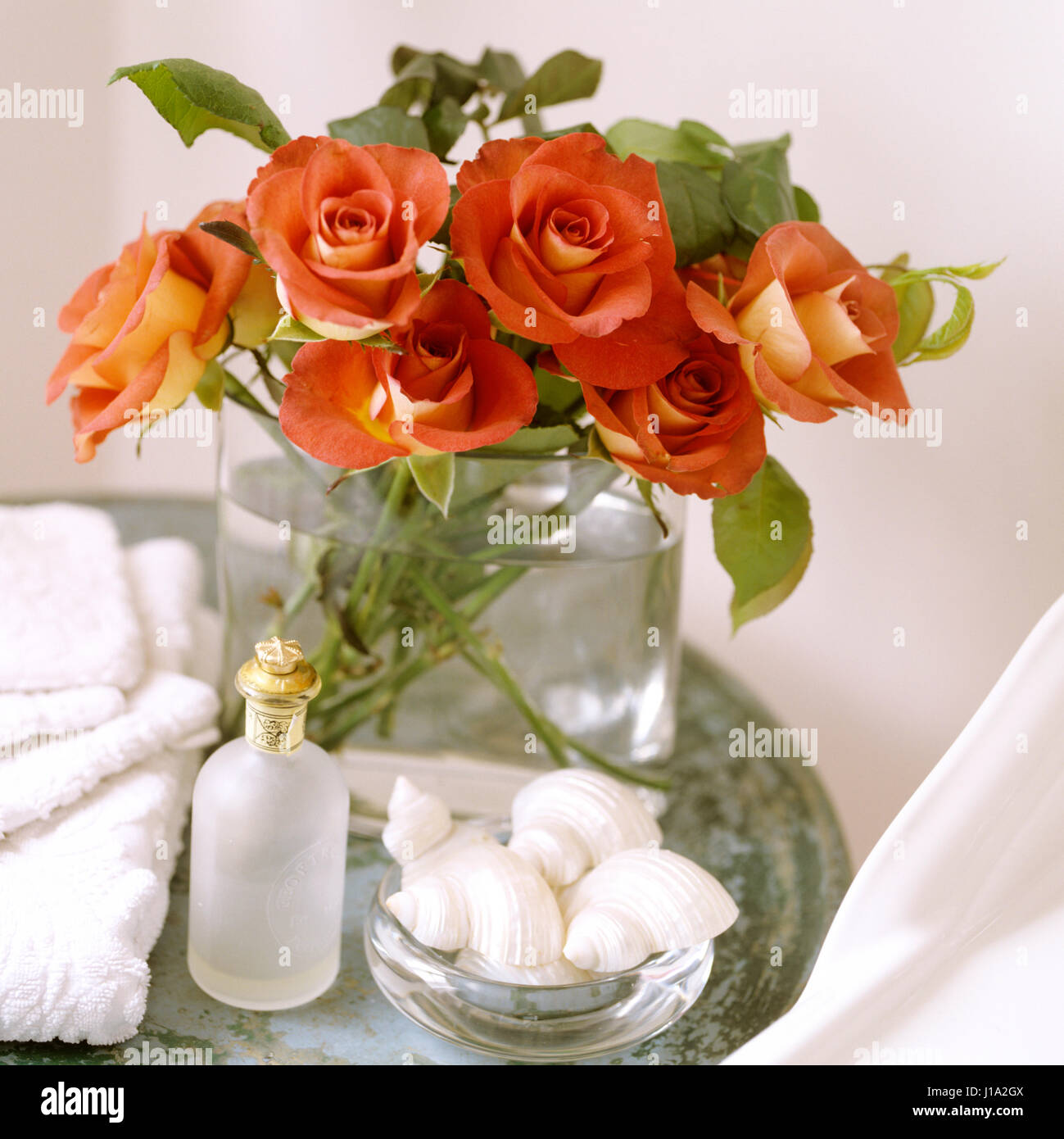 "Vase mit Blumen, Schüssel mit Muscheln, Flasche und Handtücher am Tisch." Stockfoto