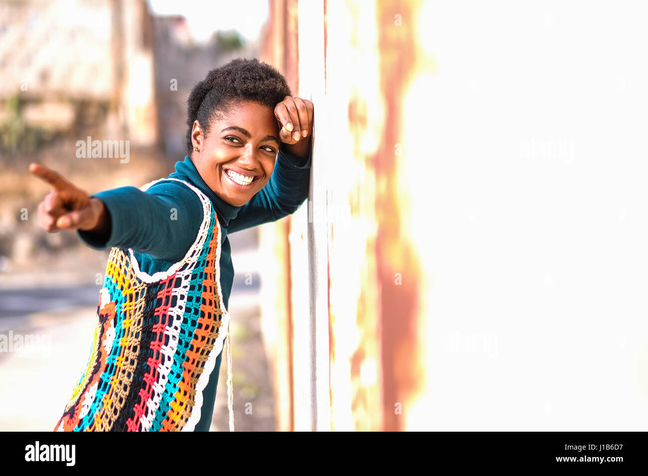 Lächelnde afroamerikanische Frau an die Wand gelehnt und Fingerzeig Stockfoto