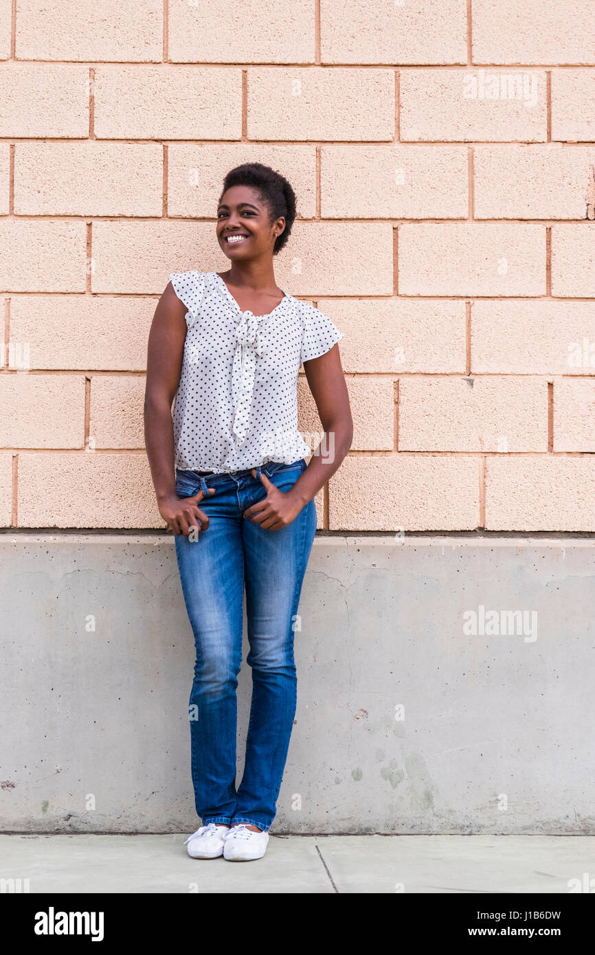 Lächelnde afroamerikanische Frau posiert in der Nähe von Betonwand Stockfoto