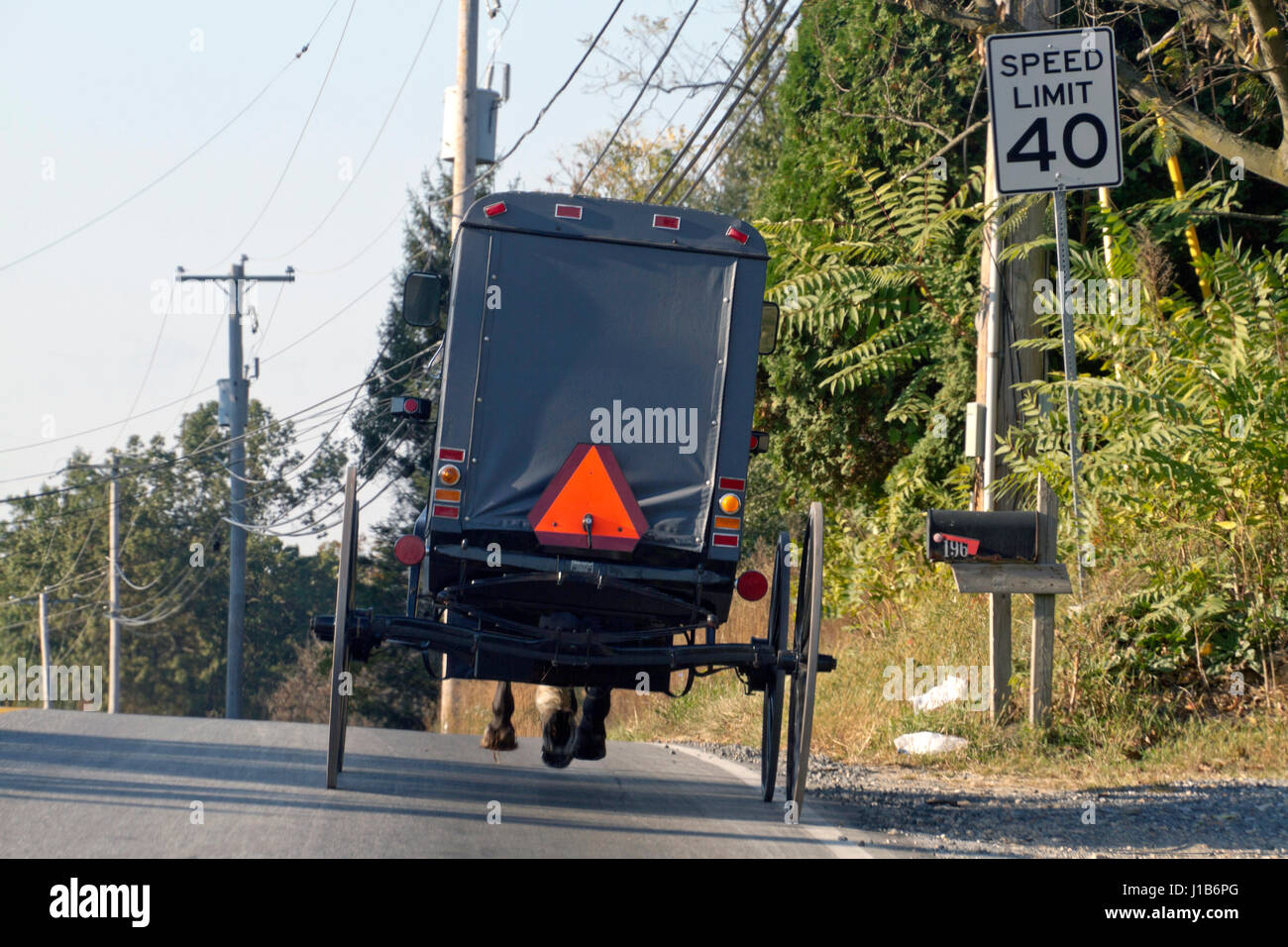 Blick auf die Rückseite ein altmodischer, Amish Pferdekutsche wie es hinunter eine Pennsylvania Landstraße vorbei an modernen Dienstprogramm Drähte, reist Telefon p Stockfoto