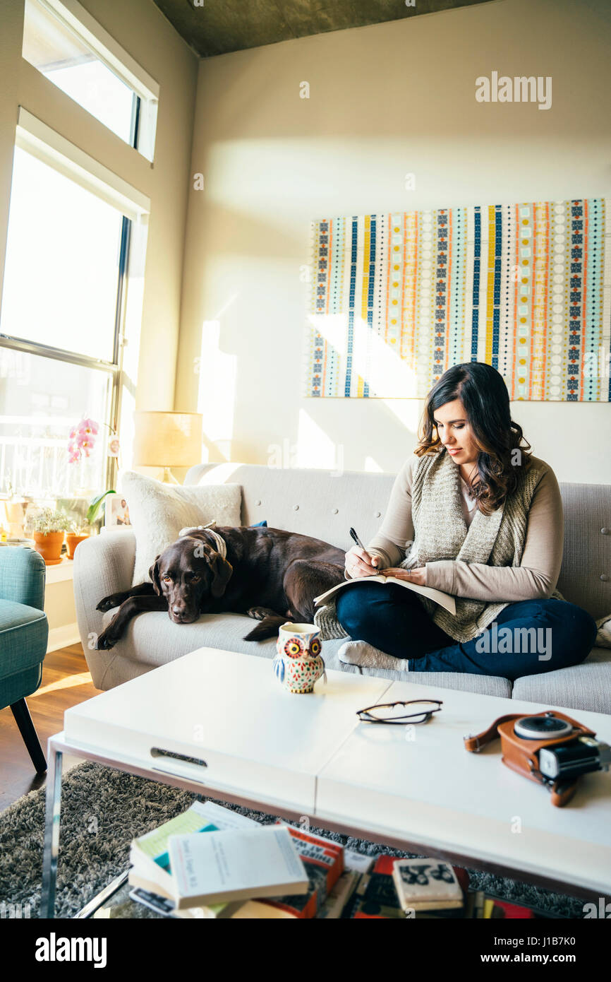 Gemischte Rennen Frau auf Sofa mit Hund in Fachzeitschrift Stockfoto