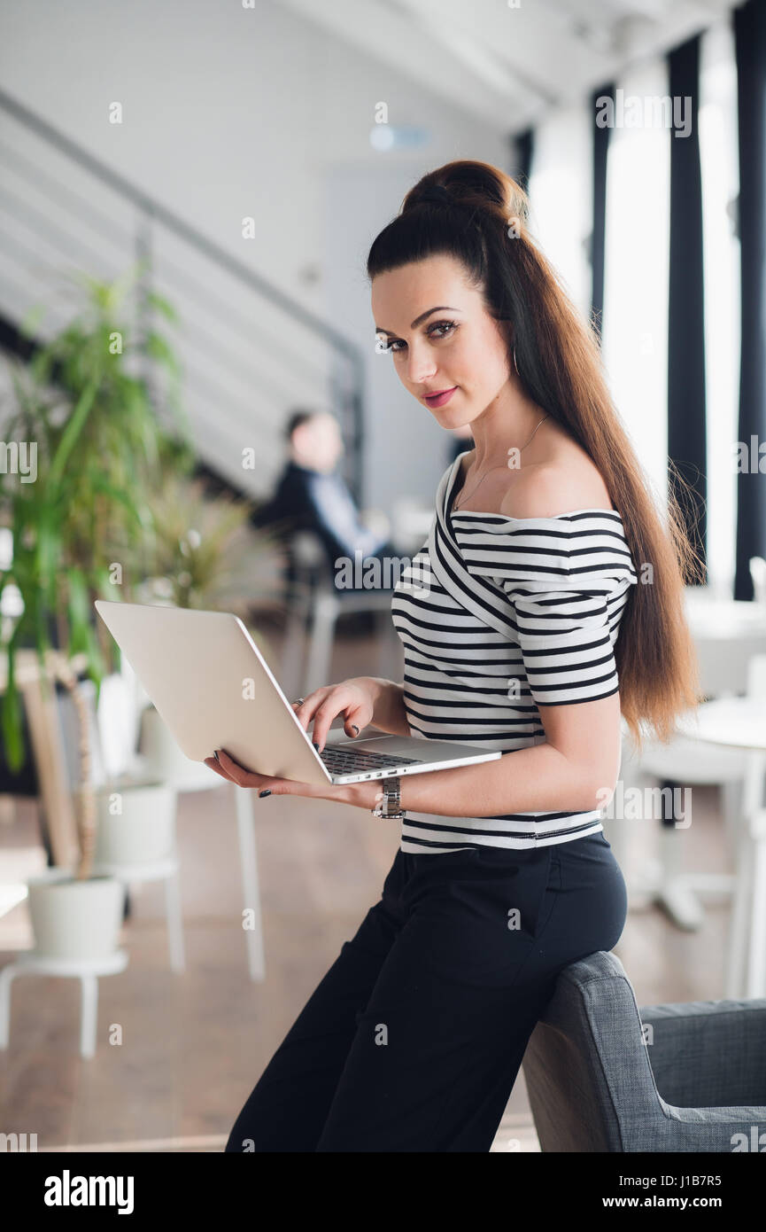 Schöne erwachsene Frau hält einen Laptop und schaut in die Kamera in einem leeren Café aufhalten. Stockfoto