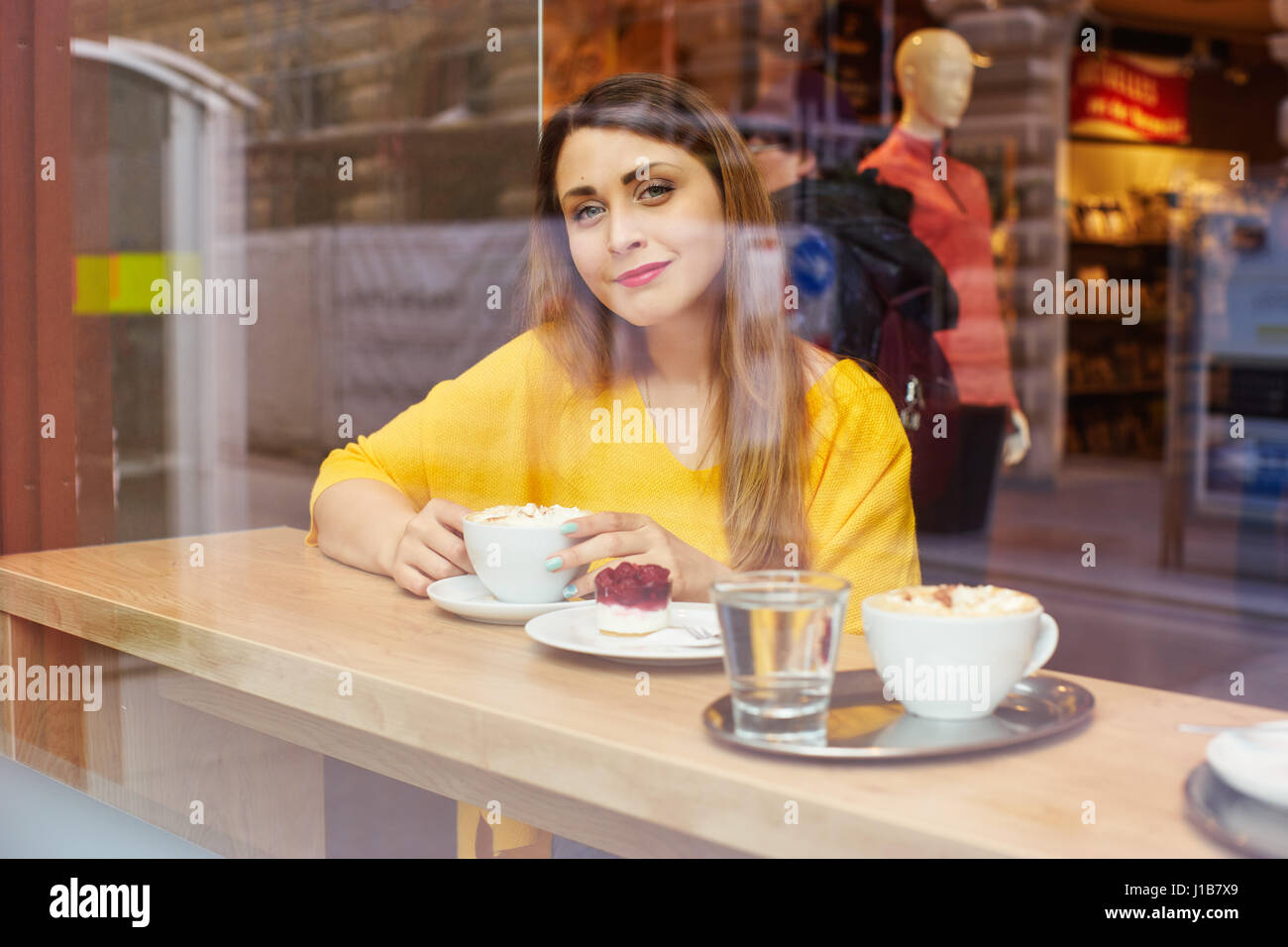 Junge, lächelnde Frau in leuchtendem Gelb Bluse im Café sitzen und schaut durch ein Fenster. Stockfoto