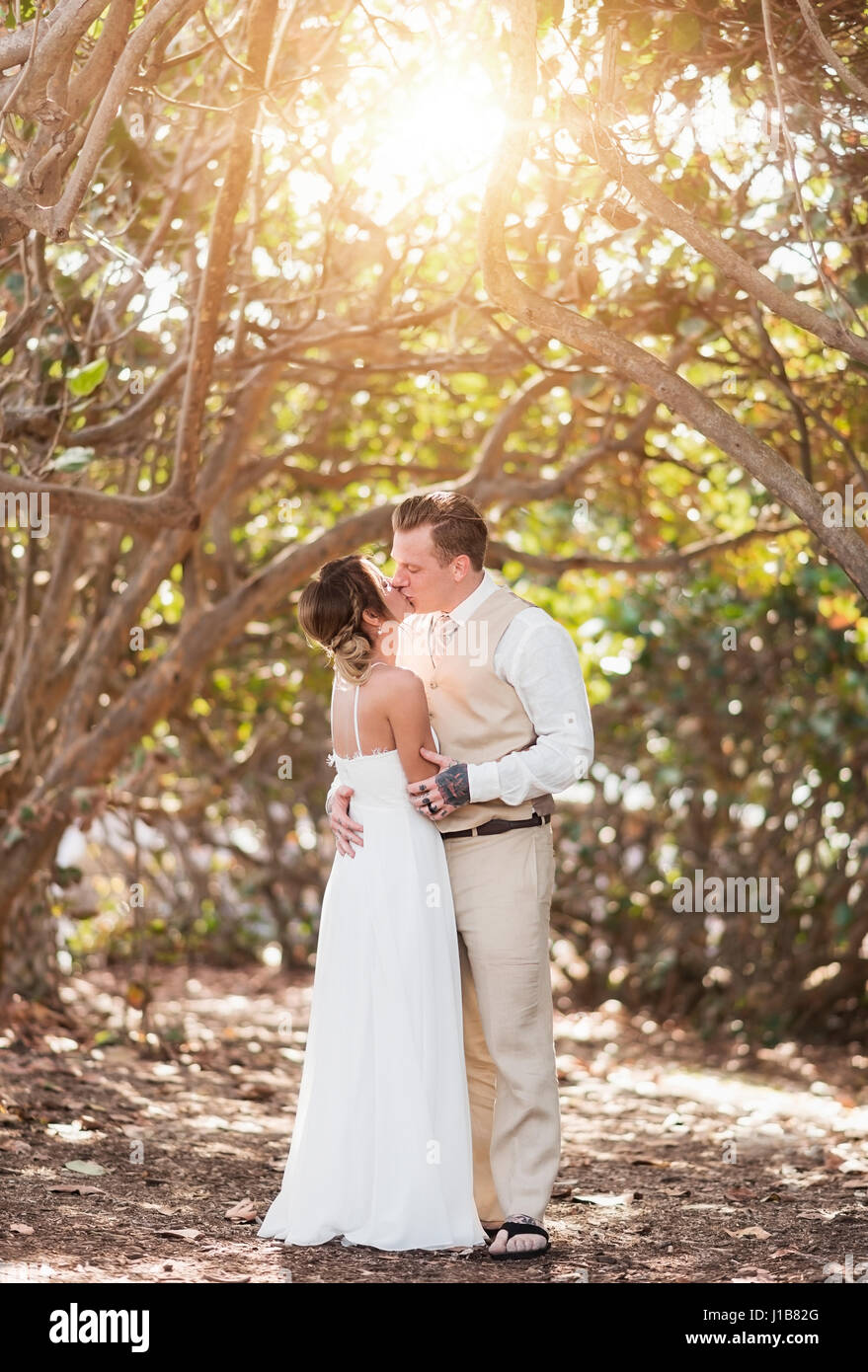Kaukasische Braut und Bräutigam küssen unter Bäumen Stockfoto