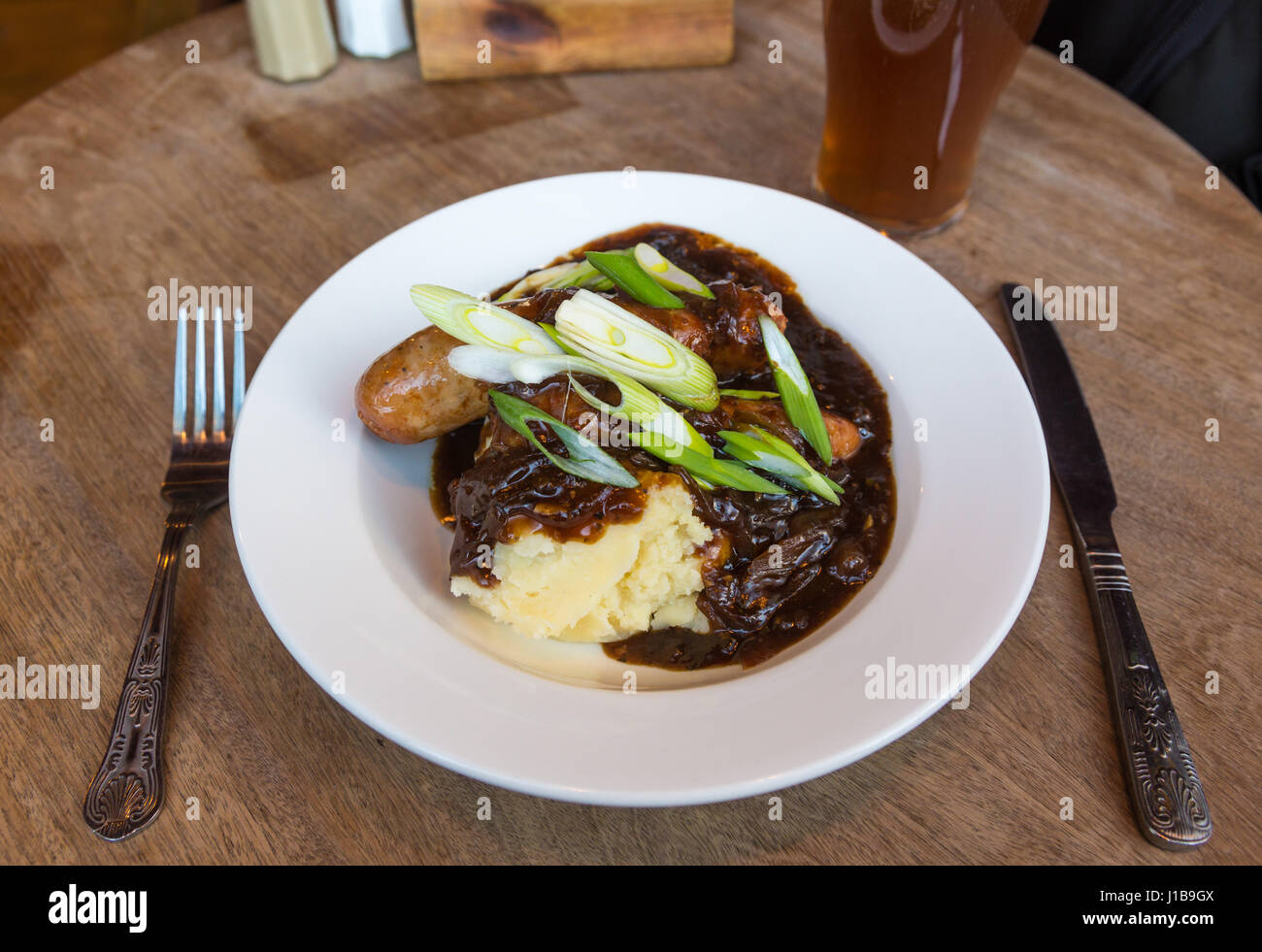 Platte des traditionellen britischen Pub essen - Teller mit Würstchen und Kartoffelbrei mit Zwiebel Soße und ein Pint Ale, Großbritannien Stockfoto