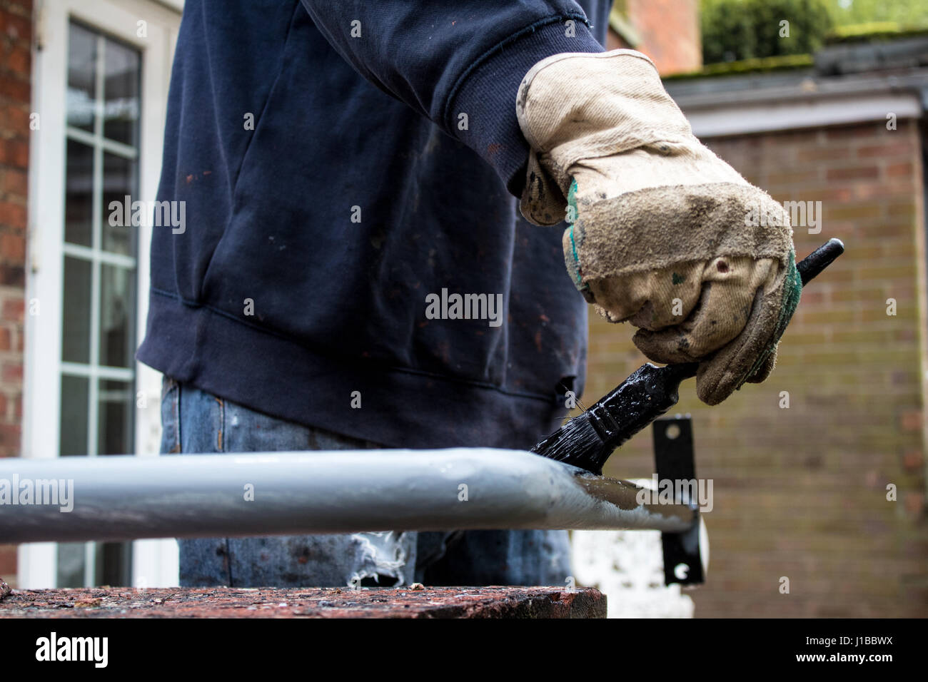 Dekorateur Schlosser Maler malt Metall Eisen Geländer schwarz mit baggy Jumper und des Arbeiters Handschuhe im hinteren Garten Wohn Job Stockfoto
