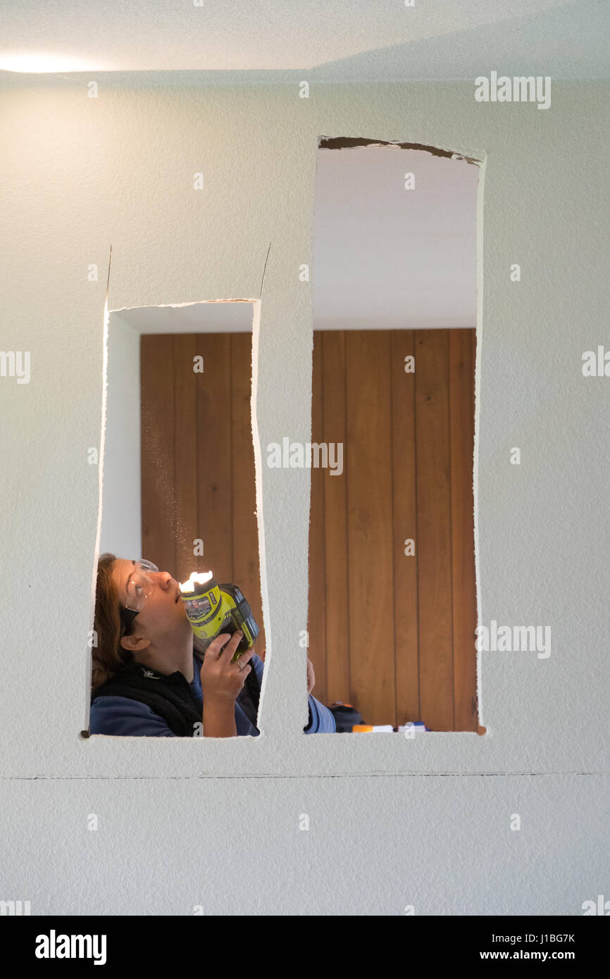 SPRINGFIELD, OR - 20. Dezember 2017: Weibliche Bauarbeiter und Hausbesitzer mit einer Taschenlampe, in einer exponierten Wand für elektrische Leitungen du suchen Stockfoto