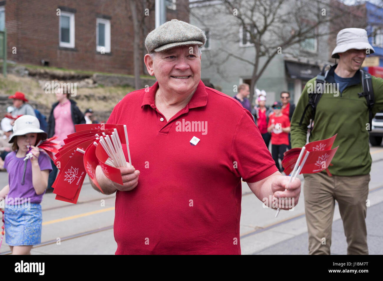 ein Alter Mann im roten T-shirt verteilt Kanada 150 Fahnen Menschen entlang der Queen Street East Strände Easter Parade 2017 Stockfoto