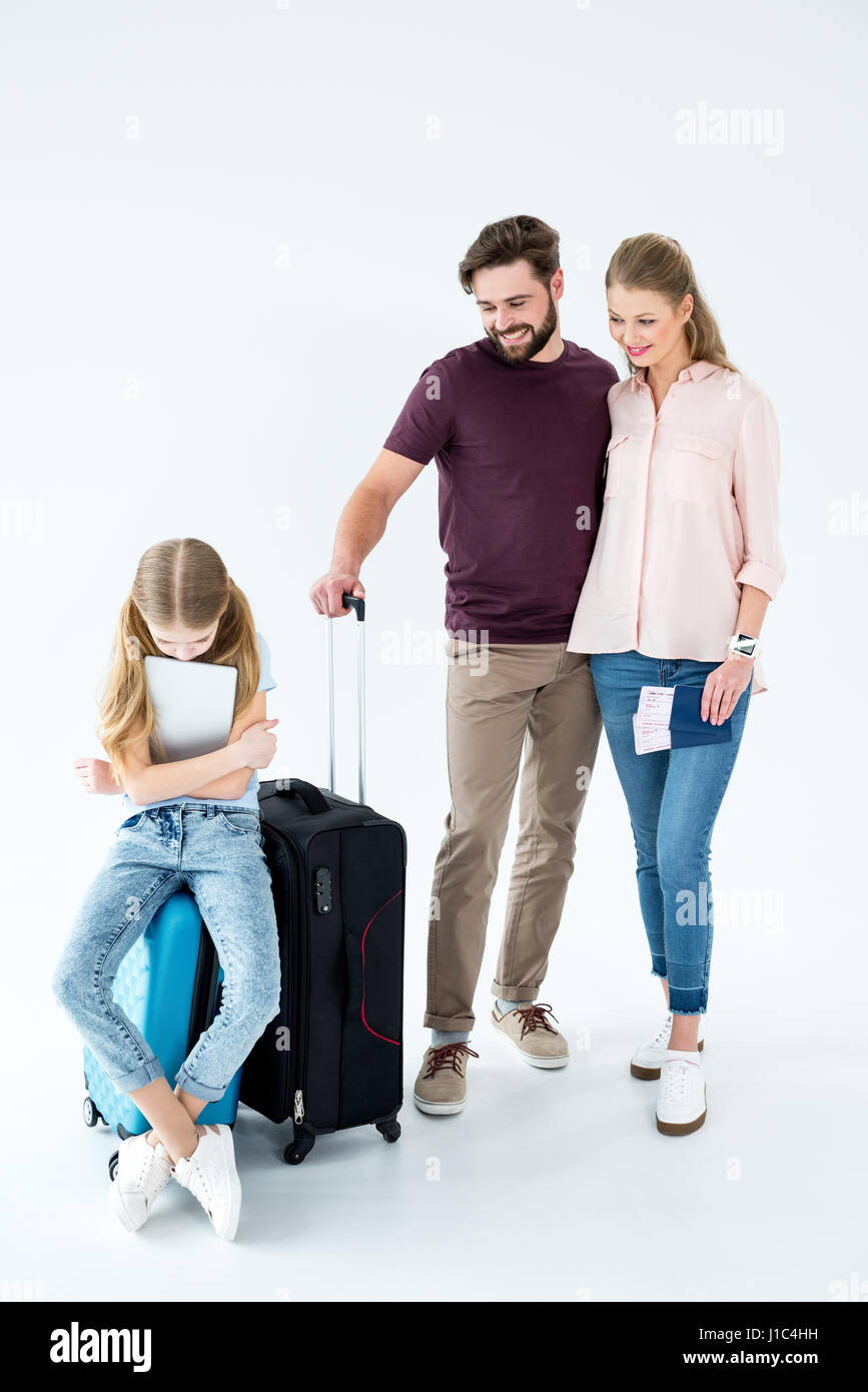 Eltern schauen aufgeregt Tochter mit Tablet sitzen auf Reisetasche auf weiß Stockfoto