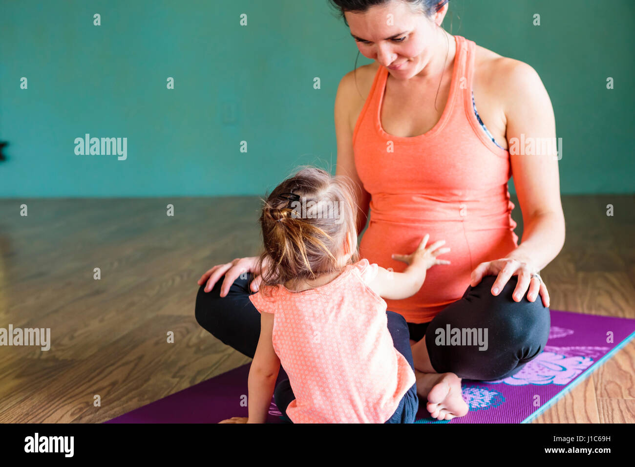 Gemischte Rennen Mädchen berühren Bauch der werdenden Mutter auf Gymnastikmatte Stockfoto