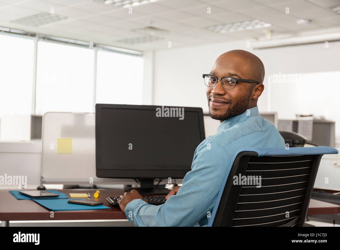 Lächelnder afroamerikanische Mann mit Computer im Büro Stockfoto